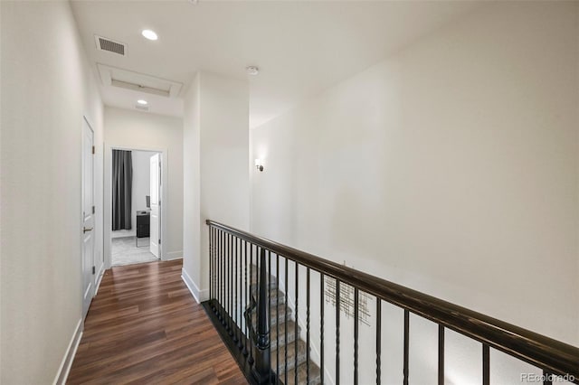 corridor with dark wood-style floors, attic access, visible vents, and baseboards