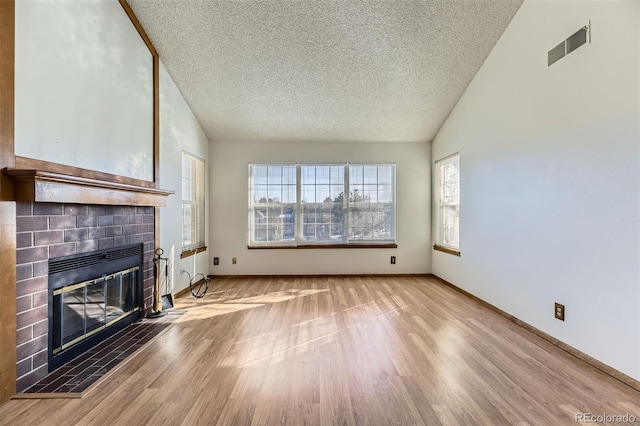 unfurnished living room featuring a tiled fireplace, a wealth of natural light, lofted ceiling, and a textured ceiling