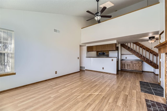 unfurnished living room with a tiled fireplace, a textured ceiling, ceiling fan, and light wood-type flooring