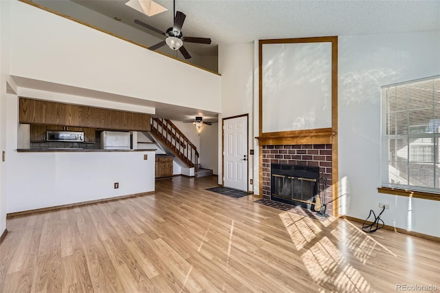 unfurnished living room with a textured ceiling, light hardwood / wood-style floors, a brick fireplace, high vaulted ceiling, and ceiling fan