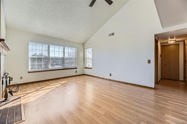 unfurnished living room with ceiling fan, light hardwood / wood-style floors, a tile fireplace, and a textured ceiling