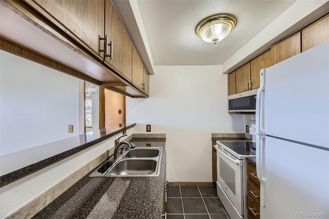 kitchen featuring white appliances, a textured ceiling, dark tile patterned flooring, and sink