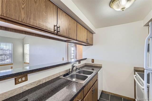 kitchen with sink, white appliances, a textured ceiling, and dark tile patterned flooring