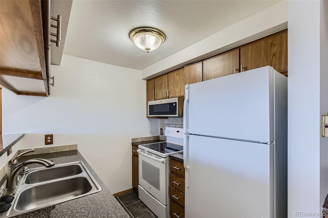 kitchen featuring white appliances, a textured ceiling, dark tile patterned floors, decorative backsplash, and sink