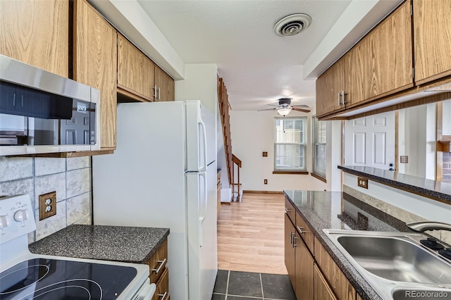 kitchen featuring white appliances, ceiling fan, dark stone countertops, and sink