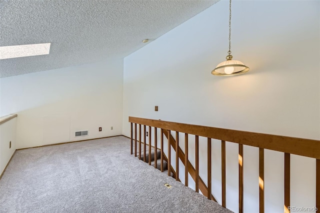 carpeted spare room featuring a textured ceiling and vaulted ceiling with skylight