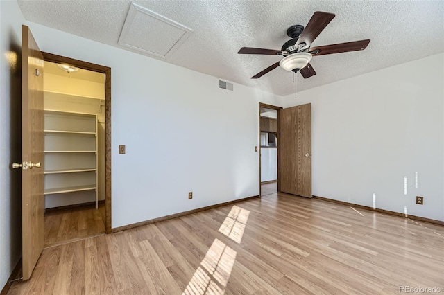 unfurnished bedroom featuring a textured ceiling, light hardwood / wood-style floors, a closet, a walk in closet, and ceiling fan