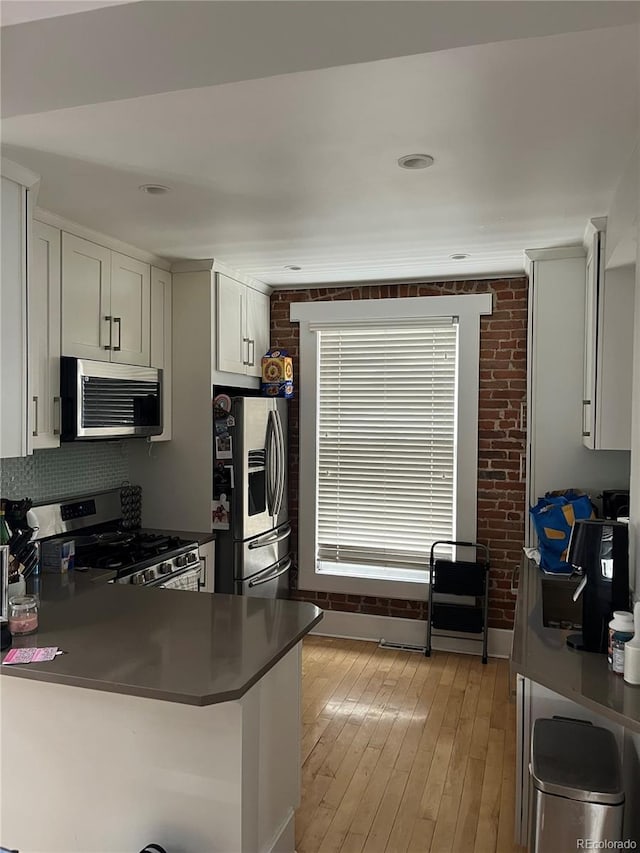 819 27th St, Denver, CO 80205 - kitchen featuring stainless steel appliances, brick wall, a peninsula, dark countertops, and light wood-style flooring