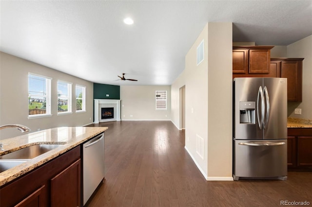1339 Sidewinder Cir, Castle Rock, CO 80108 - kitchen featuring appliances with stainless steel finishes, a ceiling fan, dark wood-type flooring, light stone countertops, and a lit fireplace
