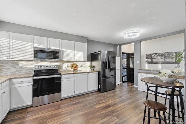 kitchen featuring tasteful backsplash, dark hardwood / wood-style floors, appliances with stainless steel finishes, white cabinets, and light stone counters