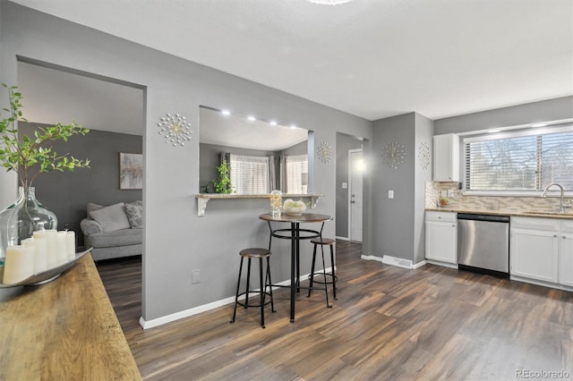 kitchen featuring tasteful backsplash, stainless steel dishwasher, a breakfast bar, sink, and white cabinetry