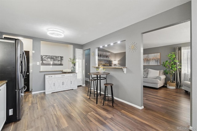 kitchen featuring white cabinets, dark hardwood / wood-style floors, a kitchen bar, and stainless steel fridge