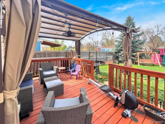 wooden deck featuring a fenced backyard, a playground, ceiling fan, and a lawn
