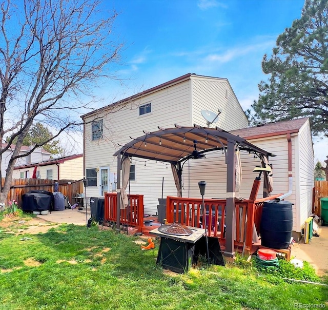 rear view of property featuring a lawn, fence, a fire pit, a patio, and a gazebo
