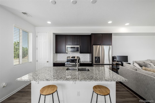 18199 E 96th Ave, Commerce City, CO 80022 - kitchen featuring stainless steel appliances, a sink, a kitchen bar, dark wood-type flooring, and light stone counters