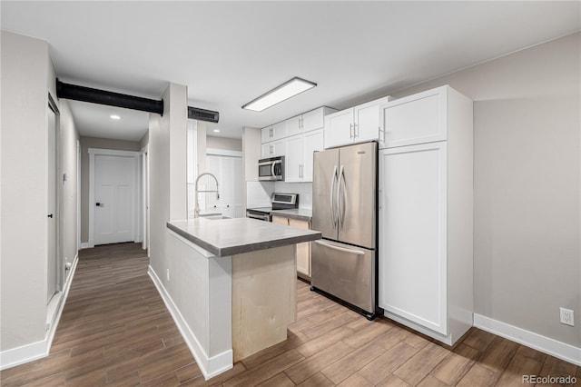 kitchen with baseboards, white cabinets, appliances with stainless steel finishes, wood finished floors, and a peninsula