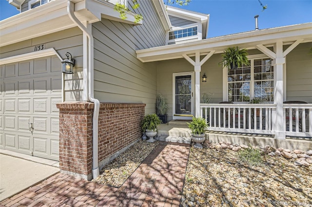 view of exterior entry featuring a porch, a garage, and brick siding