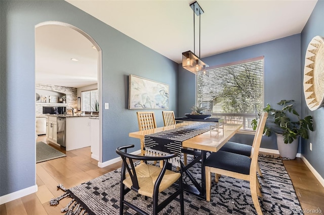 dining room featuring arched walkways, light wood-type flooring, and baseboards