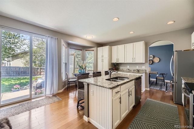 kitchen featuring a sink, appliances with stainless steel finishes, light stone counters, baseboards, and arched walkways