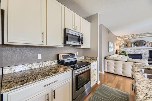 kitchen featuring appliances with stainless steel finishes, wood finished floors, open floor plan, stone countertops, and white cabinets