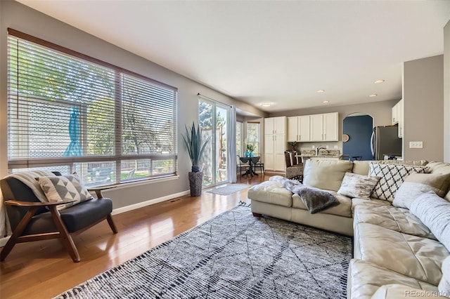 living area with arched walkways, wood finished floors, baseboards, and recessed lighting