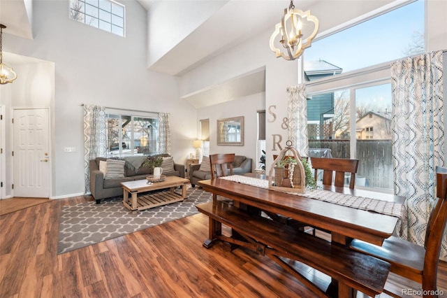 dining area featuring wood finished floors, a towering ceiling, and an inviting chandelier