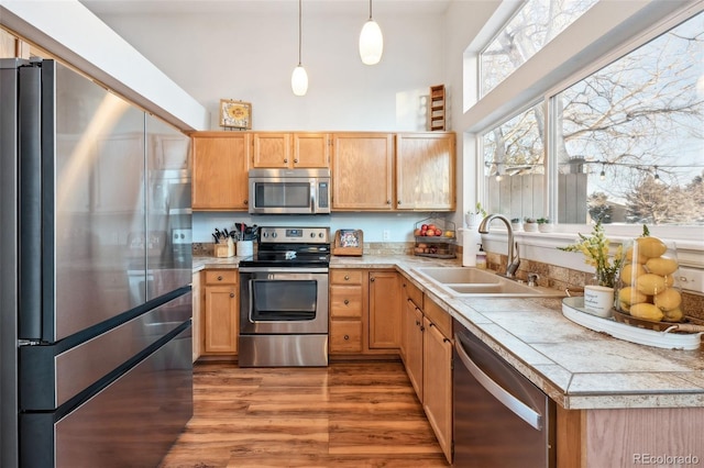 kitchen featuring pendant lighting, a high ceiling, appliances with stainless steel finishes, a sink, and wood finished floors