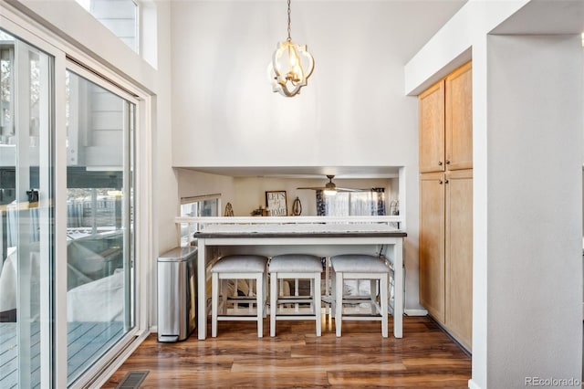 interior space with ceiling fan with notable chandelier, light brown cabinets, visible vents, and wood finished floors