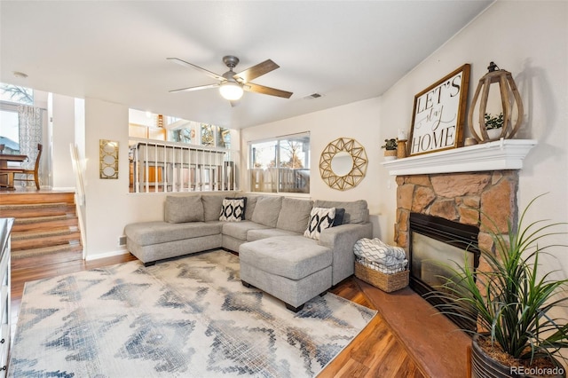 living area with baseboards, visible vents, a ceiling fan, wood finished floors, and a stone fireplace