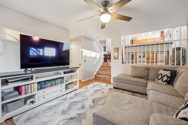 living room featuring wood finished floors, ceiling fan, and stairs