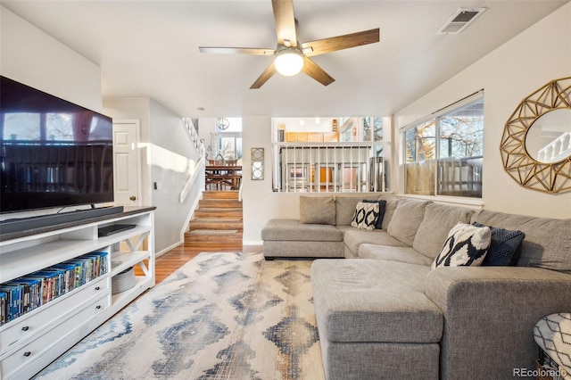 living area with a ceiling fan, visible vents, stairway, and wood finished floors