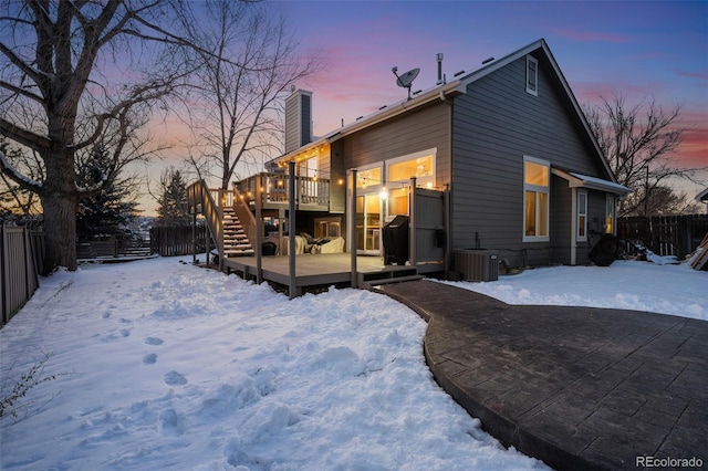 snow covered back of property featuring a deck, a chimney, a fenced backyard, and central AC