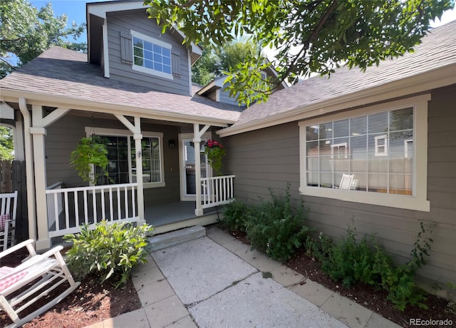 doorway to property featuring a porch and a shingled roof