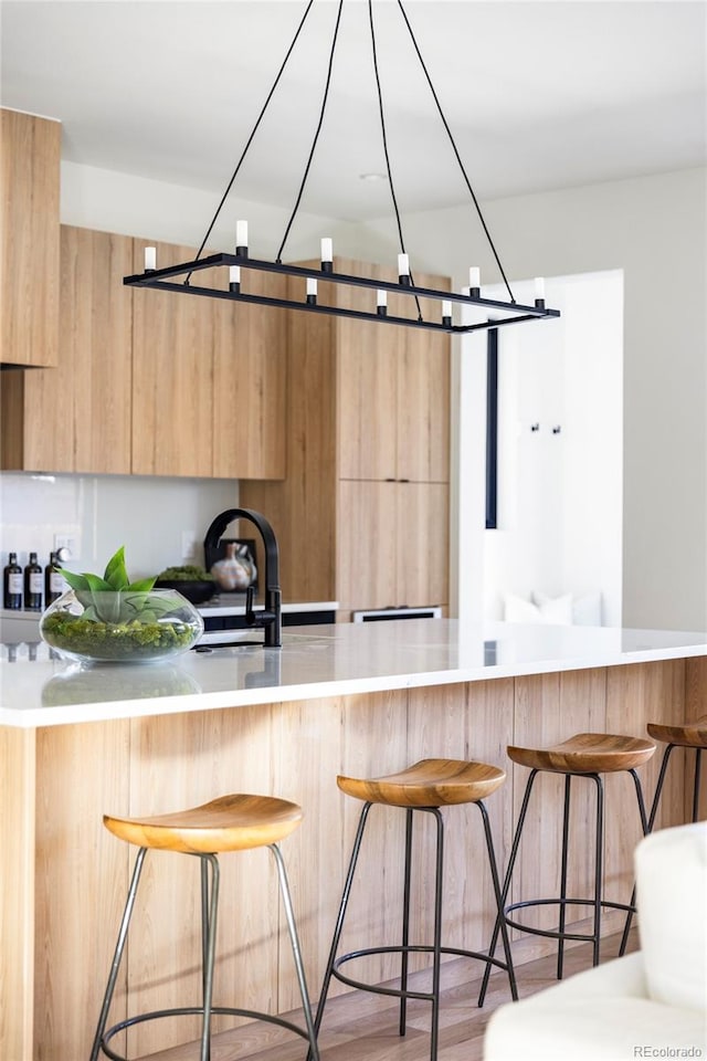 kitchen featuring sink, light wood-type flooring, a breakfast bar area, and light brown cabinetry