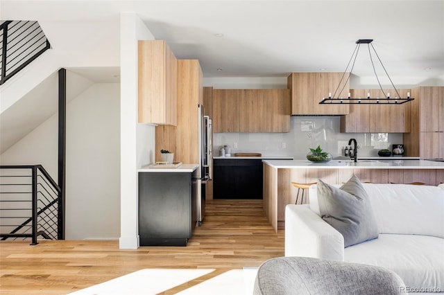 kitchen with decorative backsplash, sink, pendant lighting, and light hardwood / wood-style floors