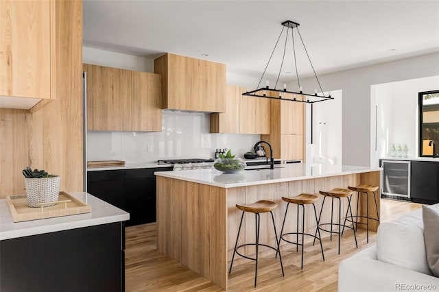 kitchen featuring light wood-type flooring, beverage cooler, sink, pendant lighting, and a center island with sink