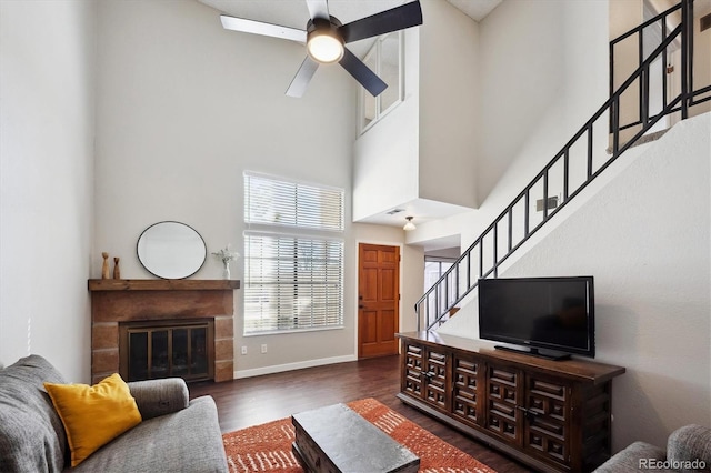 living area with a glass covered fireplace, ceiling fan, stairway, wood finished floors, and a high ceiling