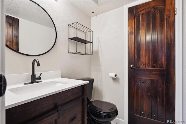 bathroom featuring toilet, a textured wall, and vanity