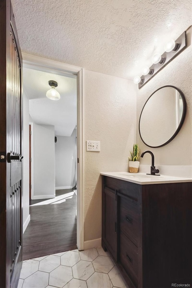 bathroom with a textured ceiling, a textured wall, tile patterned flooring, vanity, and baseboards