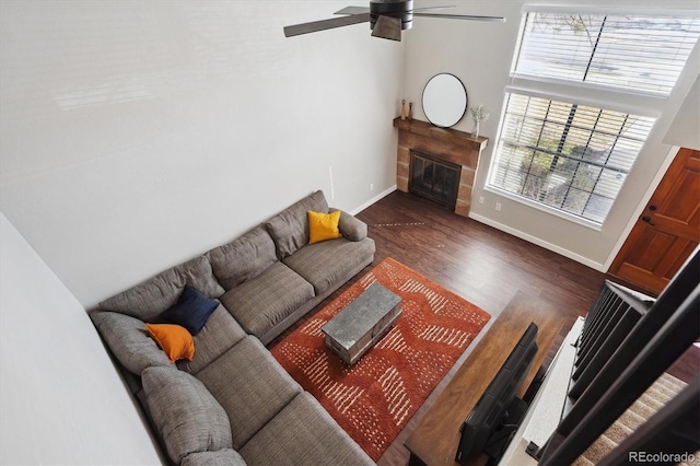 living area featuring ceiling fan, wood finished floors, a glass covered fireplace, and baseboards