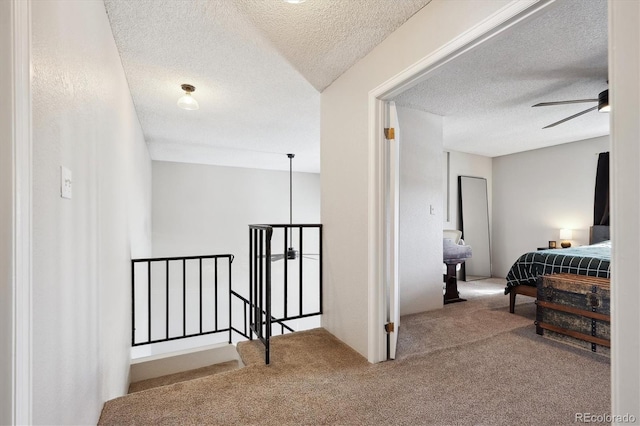 corridor with a textured ceiling, carpet flooring, and an upstairs landing