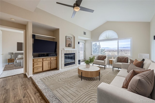 living room with a tile fireplace, ceiling fan, dark hardwood / wood-style flooring, and vaulted ceiling