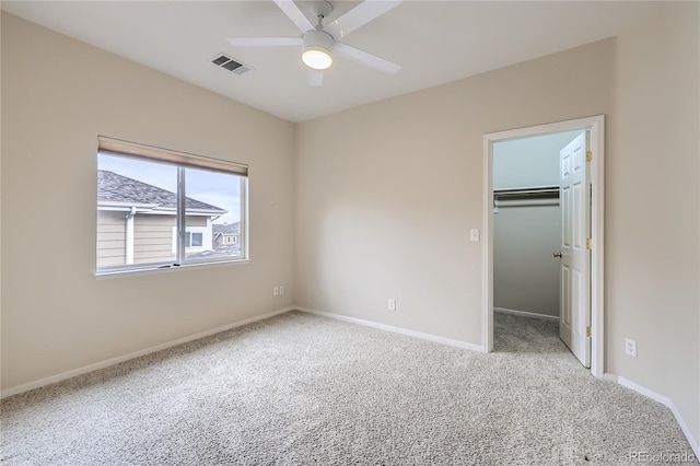 unfurnished bedroom with a walk in closet, ceiling fan, a closet, and carpet floors