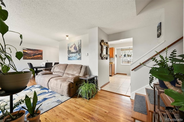 living area with stairway, baseboards, a textured ceiling, and light wood-type flooring