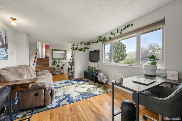 living area with baseboards, wood finished floors, a textured ceiling, and stairs