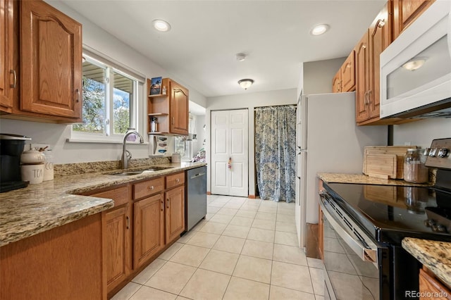 kitchen featuring brown cabinets, light stone counters, stainless steel appliances, a sink, and light tile patterned flooring