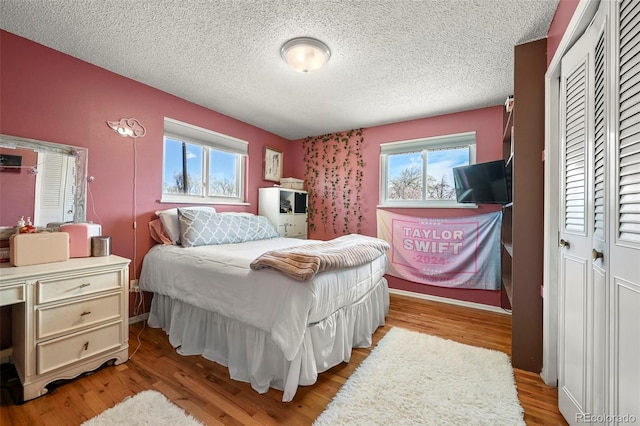 bedroom featuring a textured ceiling, light wood-style floors, a closet, and multiple windows