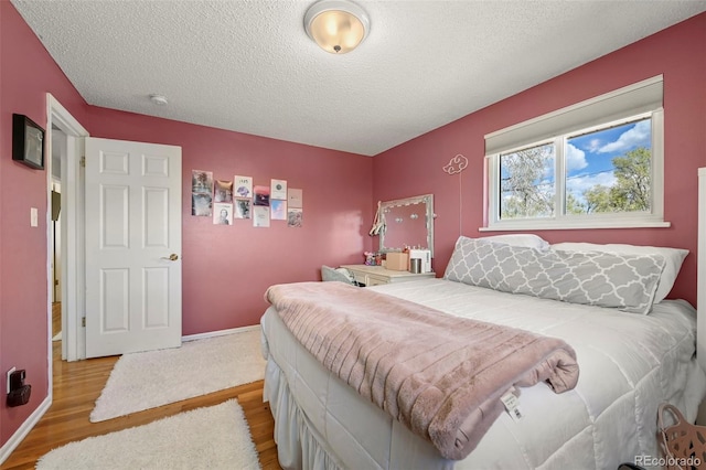 bedroom featuring wood finished floors, a textured ceiling, and baseboards