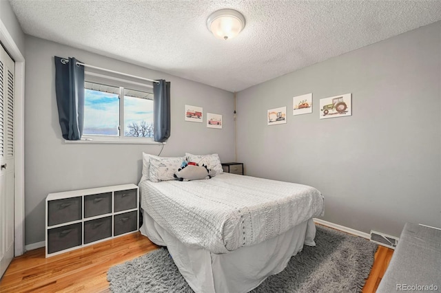 bedroom with a textured ceiling, wood finished floors, a closet, and baseboards