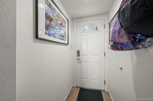 entryway with light wood finished floors, a textured wall, and baseboards
